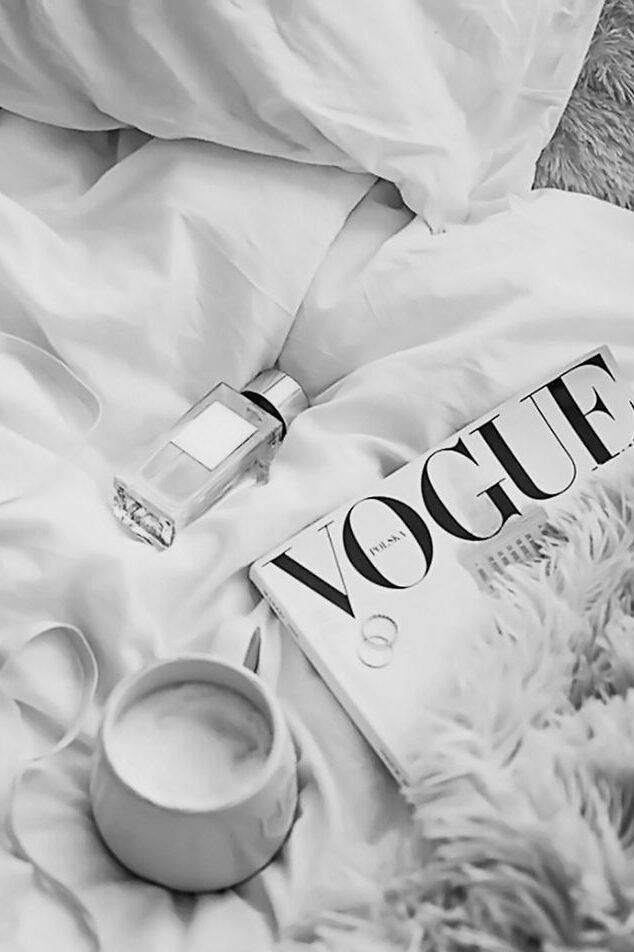Page de magazine ouverte présentant une publicité minimaliste pour un parfum de luxe, posée sur un drapé de tissu blanc soyeux, avec une mise en page épurée et des tons neutres créant une ambiance sophistiquée