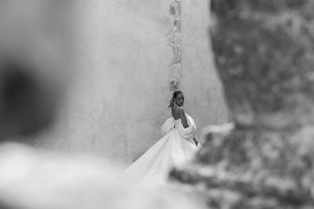 Portrait artistique capturé par un photographe de mariage du Luberon, la mariée en noir et blanc avec une robe volumineuse en mouvement, regard intense contre un mur ancien, tarif incluant ces créations artistiques personnalisées