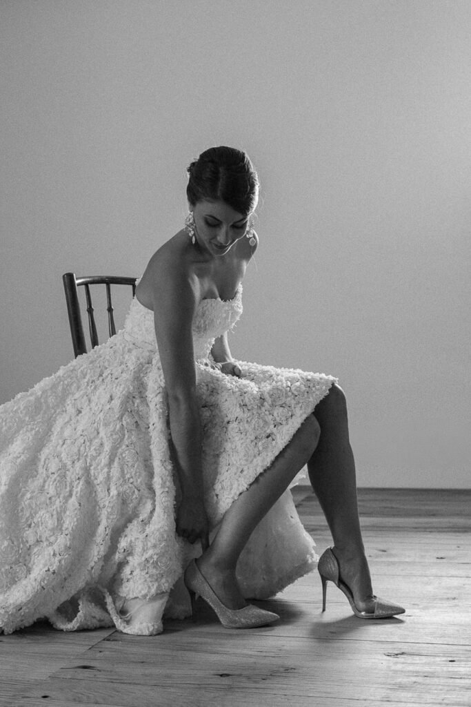 Mariée en robe de dentelle ajustant ses escarpins à talons hauts, photo noir et blanc intime