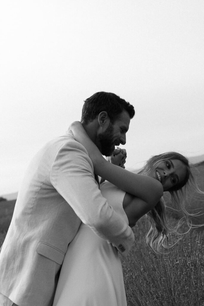 Moment de complicité entre les mariés capturé en noir et blanc par un photographe de mariage, rires authentiques au milieu des champs de lavandes en Provence, avec un tarif adapté à chaque projet.