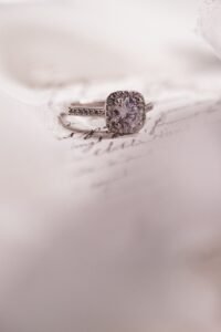 Bague de fiançailles avec diamant carré entouré de petites pierres brillantes, posée sur une lettre manuscrite ancienne avec un fond blanc doux et délicat