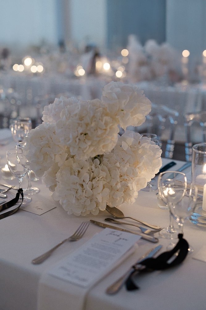 Centre de table avec hortensias blancs, bougies et menus de mariage dans une ambiance chic et tamisée.
